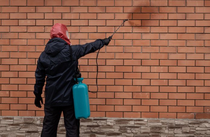 OptiCleanPlus Arbeiter in Schwarz Imprägniert die Fassade nach der Reinigung der Fassade